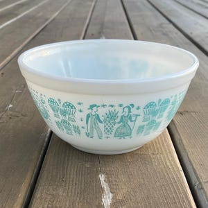 May include: White mixing bowl with a blue and green pattern of people and plants. The bowl is made of ceramic and has a smooth, glossy finish.