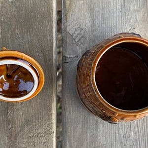 Op de afbeelding: Een bruine keramische pot met een deksel. De pot is versierd met een mandenweefpatroon en heeft een bruine glazuur. Het deksel is ook bruin en heeft een witte rand.