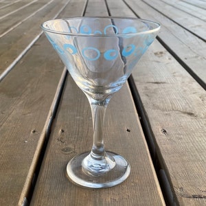 May include: A clear glass martini glass with a blue circle pattern around the rim.