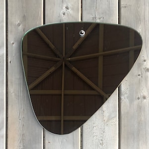 May include: A triangular-shaped mirror with a dark, reflective surface. The mirror is hanging on a wooden wall.