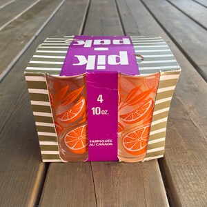 May include: A box of four 10-ounce orange juice glasses with a citrus design. The box is purple and white with the words "Pik Pak" printed on it. The glasses are made in Canada.