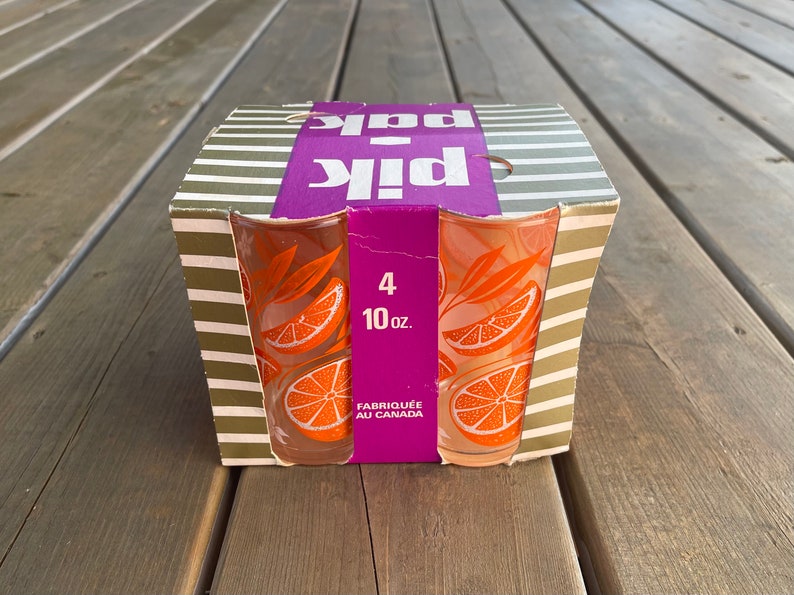 May include: A box of four 10-ounce orange juice glasses with a citrus design. The box is purple and white with the words "Pik Pak" printed on it. The glasses are made in Canada.