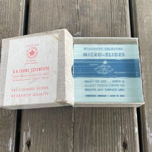 May include: A box of pre-cleaned microscope slides, labeled "STANDARD SELECTRO MICRO-SLIDES". The box is white with blue text and a blue and white image of a microscope slide. The box is open and the slides are visible inside. The box is labeled "G.H. JORNS SCIENTIFIC" and "PRE-CLEANED SLIDES RESEARCH QUALITY".