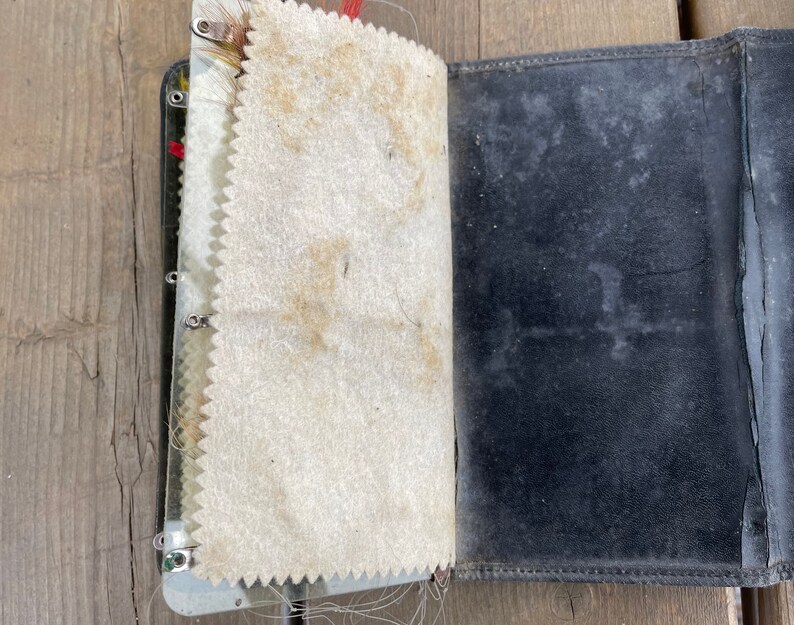 Puede incluir: Un diario de cuero negro vintage abierto, con lomo de metal y p&aacute;ginas color crema. Las p&aacute;ginas tienen un borde decorativo en zigzag. El diario muestra signos de desgaste y envejecimiento, con manchas visibles en las p&aacute;ginas y la cubierta.