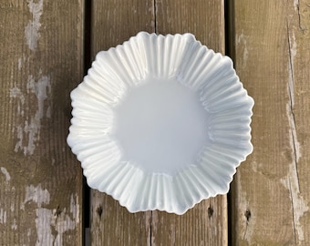 Op de afbeelding: Een witte keramische kom met een gladde, glanzende afwerking en een opvallend geschulpt, geribbeld randontwerp. De kom heeft een brede, cirkelvormige centrale kom die overgaat in een reeks stralende, verticale ribbels langs de buitenrand.