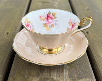 May include: A delicate teacup and saucer set with a floral design. The cup and saucer are a pale pink color with a white floral pattern and gold accents.