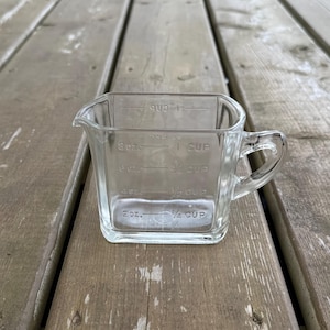 Peut inclure: Un verre doseur transparent de forme carrée avec une anse et un bec verseur. L'extérieur présente des graduations en relief indiquant 2 oz, 4 oz, 6 oz et 8 oz, ainsi que 1/4 cup, 1/2 cup, 3/4 cup et 1 cup pour les mesures impériales.