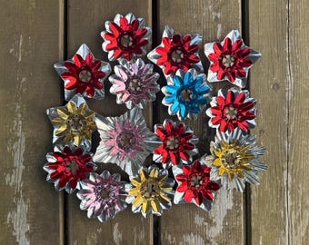 Può includere: Una collezione di riflettori in lamina metallica in stile vintage di varie forme, tra cui stelle e fiori. I pezzi presentano colori vivaci rosso, oro, blu e rosa con una finitura riflettente, ognuno con un'apertura circolare centrale.