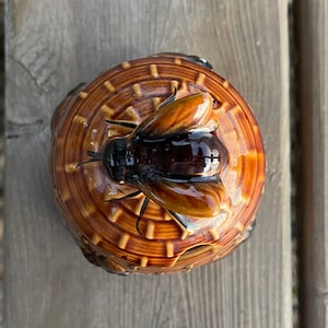 Op de afbeelding: Een keramische honingpot in de vorm van een bijenkorf, met een bruine glazuur en een bijenontwerp op de deksel.