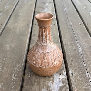 May include: A terracotta-coloured ceramic vase with a narrow neck and a rounded body. The surface features a textured, carved pattern of repeating teardrop shapes around the neck and the main body, with a matte finish and subtle white highlights.