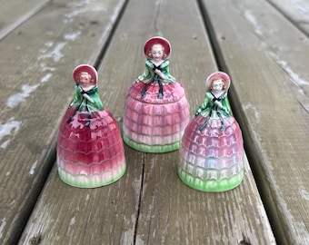 Può includere: Tre statuette in porcellana a forma di donna con ampie gonne a balze. Ogni figura indossa un corpetto verde, una cuffietta abbinata e una gonna con una sfumatura di rosa e verde. La figura centrale è leggermente più alta delle altre due.