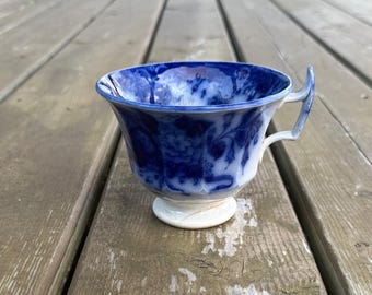 Può includere: Una tazza da tè in ceramica con un motivo floreale blu intenso e bianco. La tazza presenta un bordo svasato, una base a piedistallo e un manico dalla forma particolare. Le superfici interne ed esterne mostrano intricati motivi botanici blu.