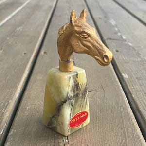 May include: A gold horse head bottle stopper with a green and black marble base. The base has the text "ONYX MAR" on it.
