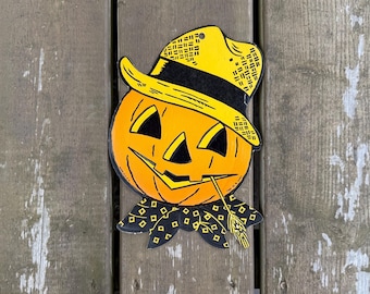Può includere: Una sagoma decorativa piatta di una zucca di Halloween che indossa un cappello giallo con una fascia nera. La zucca è arancione con occhi, naso e bocca triangolari neri. Un fazzoletto da collo nero con un motivo a rombi gialli alla base.
