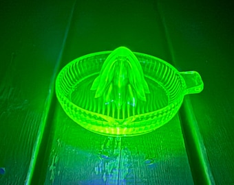 Op de afbeelding: Een levendige, oplichtende neongroene glazen citruspers met een centrale perskegel omringd door een cirkelvormig reservoir met verticale ribbels en een klein handvat aan de zijkant, verlicht voor een helder fluorescerend uiterlijk.
