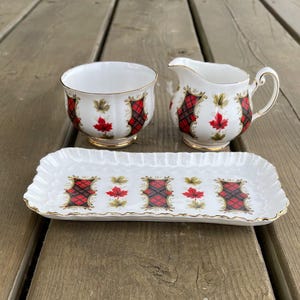 Peut inclure: Service à thé en porcelaine blanche avec un motif écossais rouge et noir et une bordure dorée. L'ensemble comprend un sucrier, une crémière et un plateau rectangulaire, décorés de feuilles d'érable.