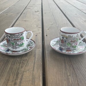 May include: Two white teacups with matching saucers. The cups and saucers feature a colourful Japanese-inspired design with red, green, and blue accents.