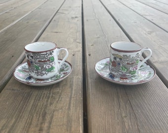 May include: Two white teacups with matching saucers. The cups and saucers feature a colorful Japanese-inspired design with red, green, and blue accents.