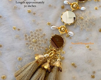 May include: A gold and white decorative hanging with multiple small mirrors, white seashells, and gold tassels. The hanging is approximately 76 cm long. Light weight.