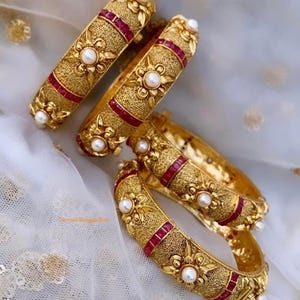 Bracciale rigido a vite con finitura dorata e accenti di perle/rubini, ideale per matrimoni, feste e regali, stile indiano/pakistano.