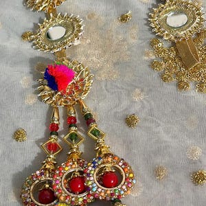 May include: A set of colorful tassel embellishments with gold accents. Each tassel features a round mirror surrounded by a gold frame, a pom-pom, and a beaded chain.