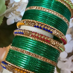 Könnte beinhalten: Ein Stapel grüner Glasarmbänder mit goldenen und Strass-Akzenten. Die Armbänder sind mit bunten Streifen und Perlen verziert.