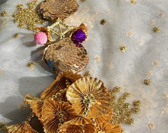 May include: A gold and colourful decorative trim with multiple layers of gold fabric, sequins, and pom-poms. The trim features a variety of colours, including red, orange, yellow, green, blue, and purple.