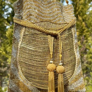 Puede incluir: Un bolso de noche de cuentas doradas y plateadas con una correa de cadena y detalles de borlas.