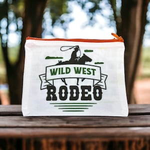 May include: White canvas zippered pouch with a graphic of a cowboy riding a horse and the text "Wild West Rodeo".