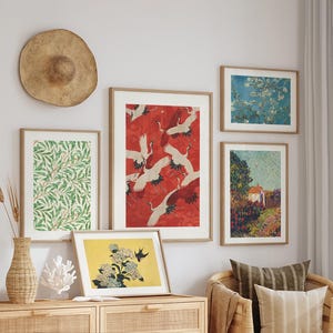 May include: A gallery wall arrangement featuring five framed art prints: a green leaf pattern, a red crane print, a yellow floral print, a blue blossom print, and a garden landscape. A round straw hat hangs above the prints near a woven vase.