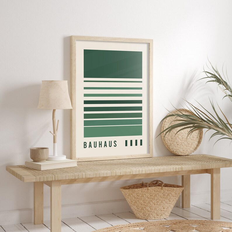 May include: A rectangular wall art print in a light wood frame featuring a cream background with horizontal stripes in varying shades of green. The text "BAUHAUS" is printed in black at the bottom left, followed by four small black vertical rectangles.