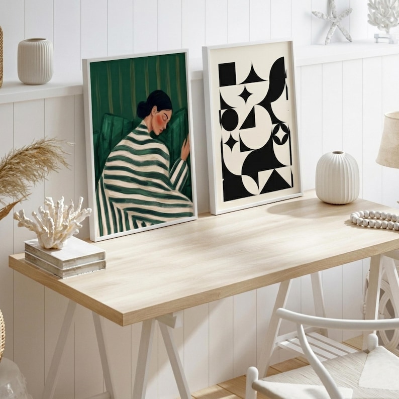 Op de afbeelding: Twee ingelijste rechthoekige kunstprints op een bureau van licht hout. De linker print toont een persoon in een groen-wit gestreept kledingstuk tegen een groene achtergrond. De rechter print toont een zwart-wit geometrisch patroon.