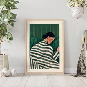 A framed art print featuring a person in a striped robe, resting on a green sofa. The artwork has a serene, calming aesthetic, with a color palette of green, white, and beige. The person's face is painted with soft, warm tones.