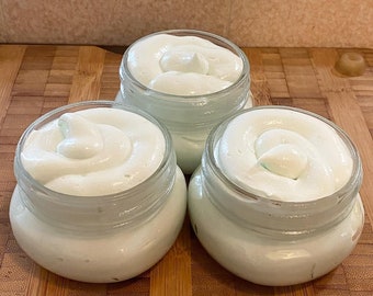 May include: Three glass jars filled with a light green whipped cream. The jars are sitting on a wooden surface.