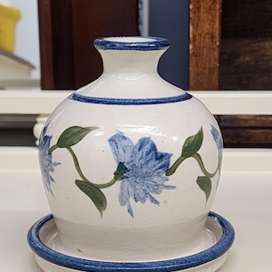 May include: A white ceramic vase with a blue rim and blue floral design. The vase has a matching saucer.