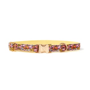 May include: A yellow dog collar with a floral print featuring pink, orange, and white flowers. The collar has a gold metal buckle and a gold metal D-ring.