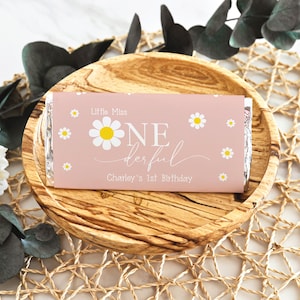 May include: Pink chocolate bar wrapper with white daisies and the text "Little Miss One-derful Charley's 1st Birthday"