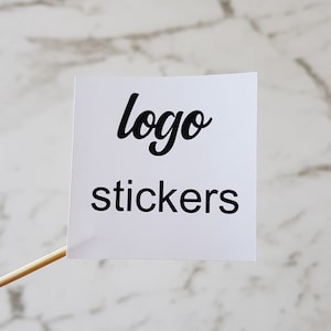 May include: White square sticker with black text that reads "logo stickers".