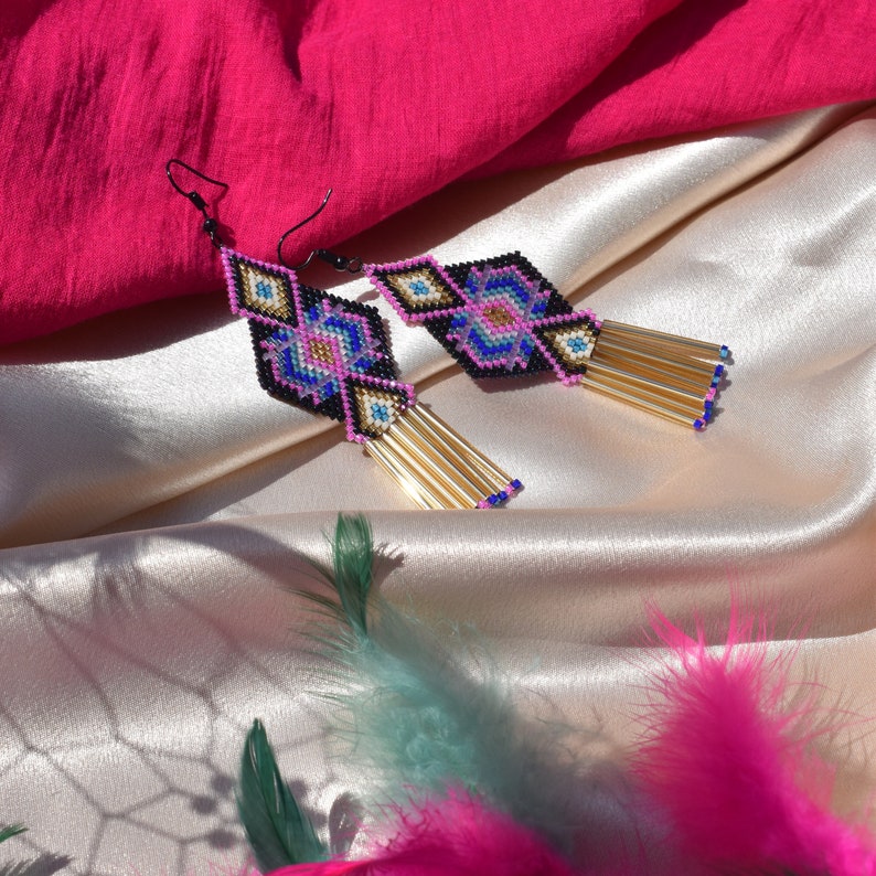 May include: A pair of long, beaded earrings with a geometric pattern in shades of pink, blue, black, and gold. The earrings have a tassel of gold beads.