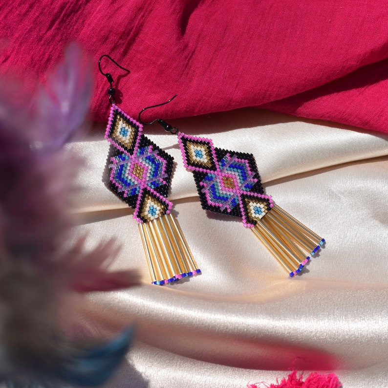 May include: A pair of geometric beaded earrings with a pink, blue and gold colour scheme. The earrings feature a diamond-shaped design with a tassel of gold beads.