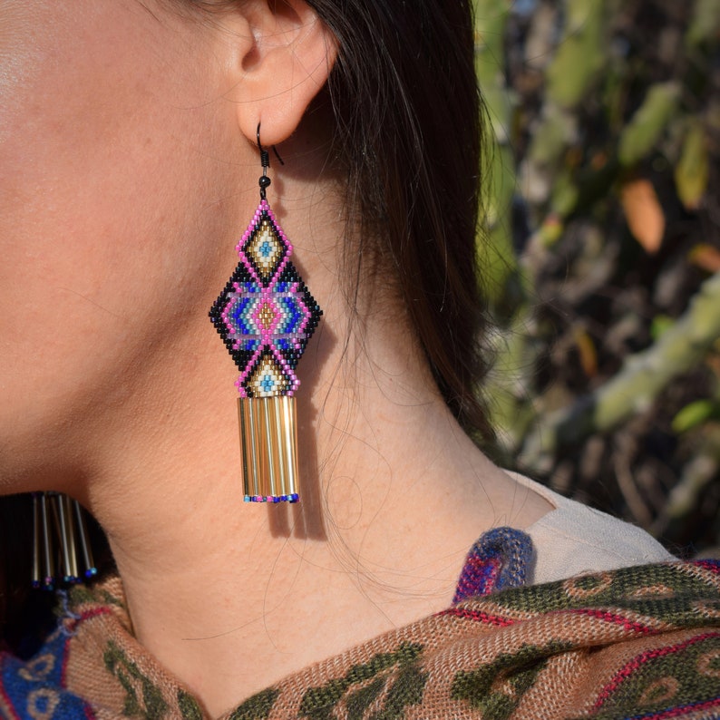 May include: A pair of dangle earrings with a geometric design in pink, blue, gold, and black. The earrings have a tassel of gold beads.