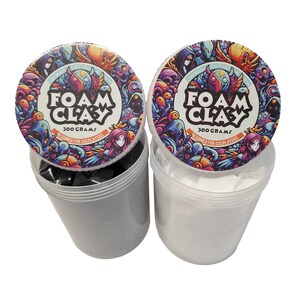 Pu&ograve; includere: Due contenitori di argilla di schiuma nera e bianca, ognuno con un coperchio colorato che presenta un design di cartoni animati e il testo "Foam Clay 300 Grams Designed for Cosplayers".