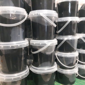 Pu&ograve; includere: Una pila di secchi di plastica neri con coperchi e manici trasparenti. I secchi sono pieni di una sostanza nera.