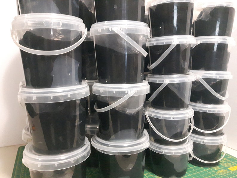Pu&ograve; includere: Una pila di secchi di plastica neri con coperchi e manici trasparenti. I secchi sono pieni di una sostanza nera.