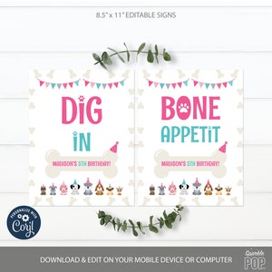 May include: Two printable 8.5 x 11 inch signs for a dog-themed birthday party. The signs are white with a light brown bone shape at the bottom. The first sign says "Dig In" in pink and teal with a pink paw print and a party hat. The second sign says "Bone Appetit" in pink and teal with a pink paw print and a party hat. Both signs have a row of cartoon dogs wearing party hats at the bottom.