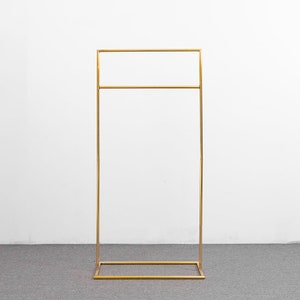 May include: A gold metal clothing rack with a rectangular base and two horizontal bars. The rack is standing on a gray carpet.