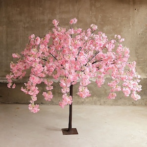Puede incluir: Un &aacute;rbol artificial de cerezo en flor rosa con un tronco y ramas negras. El &aacute;rbol est&aacute; en plena floraci&oacute;n y las flores caen en cascada.