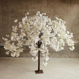 Puede incluir: Un &aacute;rbol artificial de cerezo en flor blanco con un tronco marr&oacute;n y una base de metal. El &aacute;rbol tiene muchas ramas con flores blancas que caen en cascada.