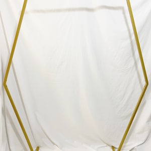 May include: Gold metal hexagonal archway stand for wedding or event decor. The stand is made of sturdy metal and has a simple, elegant design.