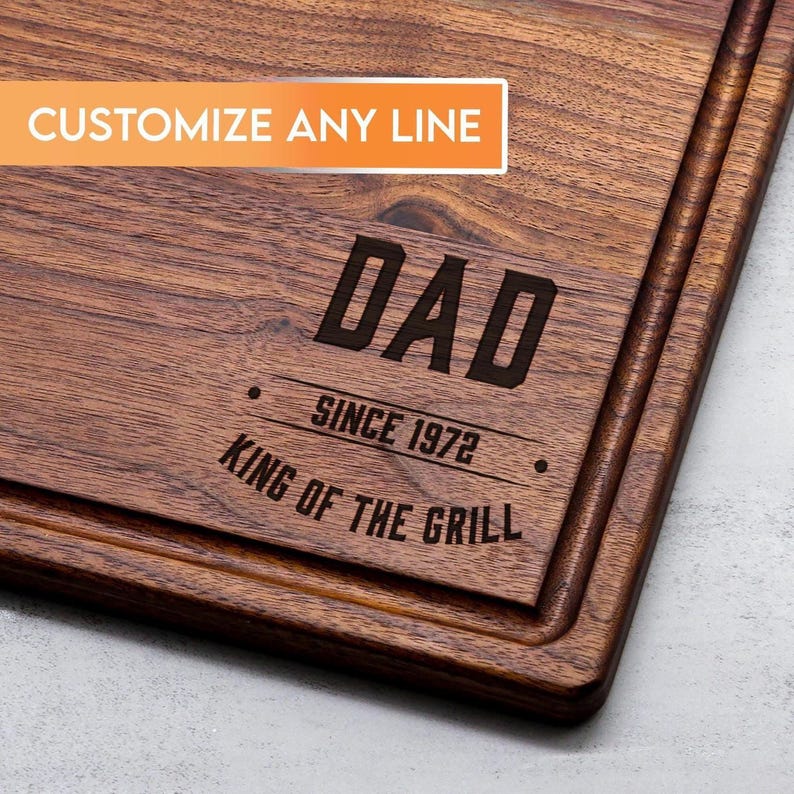 A wooden cutting board with the text "DAD SINCE 1972 KING OF THE GRILL" engraved on it.
